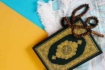 The Holy Quran with a prayer mat and tasbih on a blue and yellow background