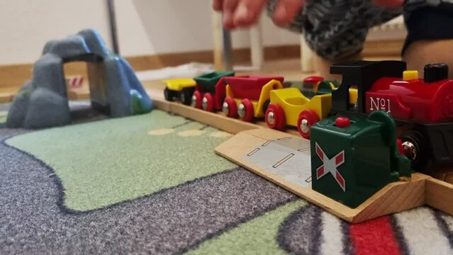 A faceless child playing with colorful wooden train, moving it back and forth in the wooden train rail.