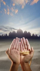 Foto op Plexiglas Muslim man's hand holding prayer beads is praying to Allah with a mosque and desert in the background. © Leo Lintang