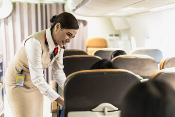 Friendly Asian female airhostess taking care passenger on plane