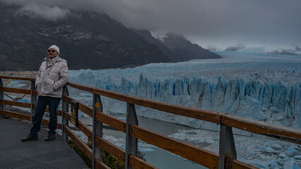 A man in a down jacket and a hat stands on the observation deck at the Perito Moreno glacier,...