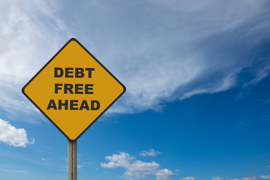 Image of yellow road sign with debt free ahead written on it with blue sky background.
