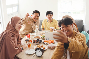 Young muslim friends taking selfie or video call during eating together. Iftar ramadhan and eid...