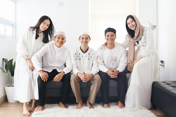 Portrait of young Asian muslim people wearing traditional islamic clothes, sitting on couch and...