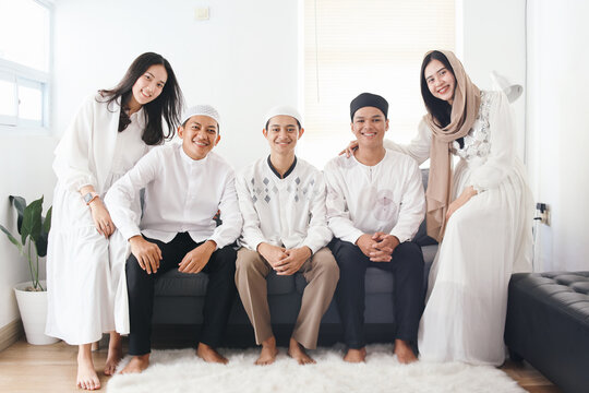 Portrait of young Asian muslim people wearing traditional islamic clothes, sitting on couch and looking at camera smiling