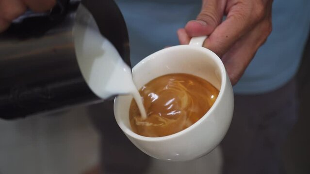 Barista pouring milk to make coffee latte art. b-roll footage video 4k. Cafe business shop. Professional man making pouring steamed milk with espresso to make latte art coffee. Cappuccino.