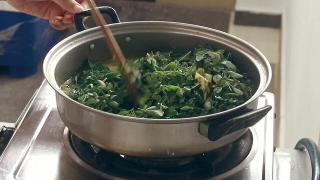 Mixing and stirring moringa leaves or malunggay to cook ginataang gulay or coconut milk vegetable stew, a vegan traditional Filipino dish