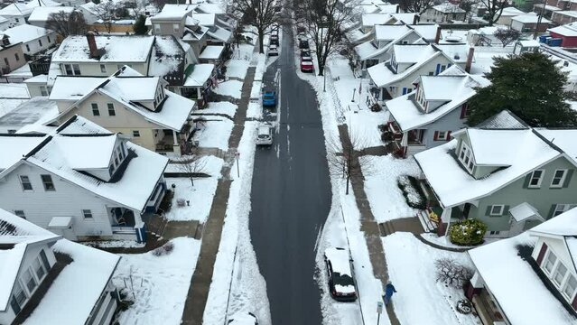 Person clearing sidewalk full of snow in american housing area. Winter snow with parking cars in United States. Aerial Birds Eye shot.