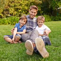 Naklejka na ściany i meble Smile, nature and portrait of children with father relaxing on grass in outdoor park or garden. Happy, family and excited cute boy kids sitting on lawn with young dad for bonding in field together.
