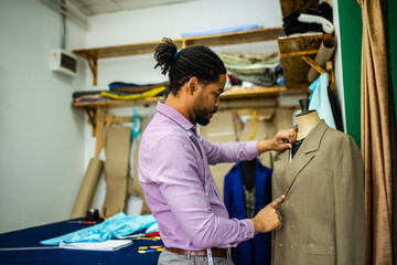 Male African American tailor measuring the suit with measuring tape.