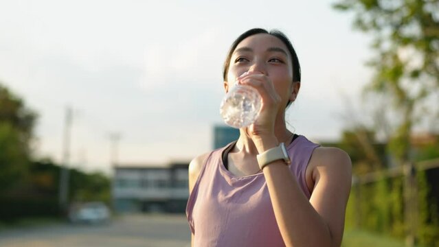 Confident young Asian woman running outdoors along the village street. Stand and drink water to cool down. healthy lifestyle and sports concepts Use your free time to your advantage.