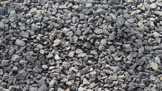 Panning shot of gray, white and dark rocks ang gravel with some leaves and twigs in slow motion.