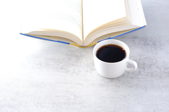 テーブルの上の開いた本と、コーヒーの入ったコーヒーカップで、コーヒーを飲みながら読書を楽しむイメージ
