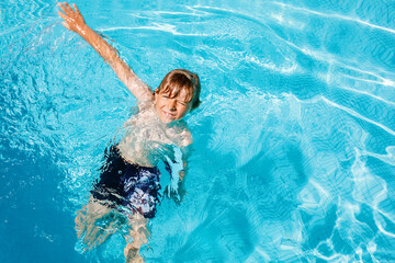 Portrait of happy little kid boy in the pool and having fun on family vacations in a hotel resort. Healthy child playing in water, swimming and splashing.