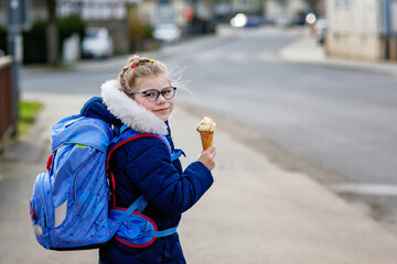 Cute little girl o the way home from school. Healthy happy child with eyeglasses with ice cream...