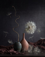 Modern still life with a large dandelion in a clay vase on a dark background