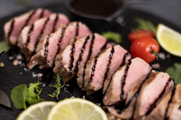 sliced grilled cooked piece of tuna fillet on black stone serving board