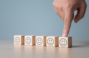 Hand chooses smiley happy face on wooden cube from normal to sad emotion on others. World Mental Health Day, Feedback rating, Customer service review. Think positive and satisfaction survey concept.
