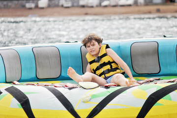 Young boy exudes joy while riding an inflatable tube towed by a boat in the ocean. Happy school child having fun in adventure water park on the sea.