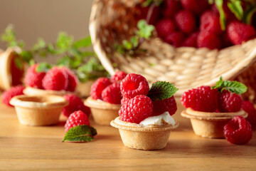 Tartlets with fresh raspberries and mint on a wooden table.