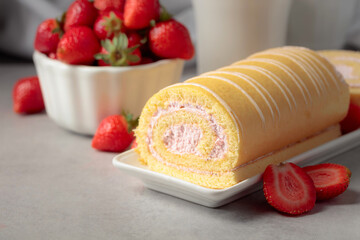 Delicious biscuit roll cake with fresh strawberries on a white stone table.