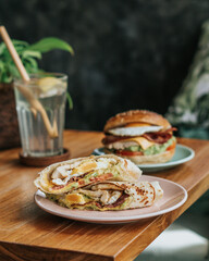 A burrito and burger with eggs, salsa verde, sour cream, and maple syrup on wooden table and drink