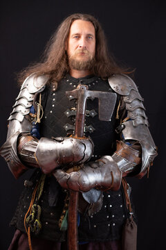 Vertical composition. Portrait of a medieval knight with an axe and protective iron handles on a black background