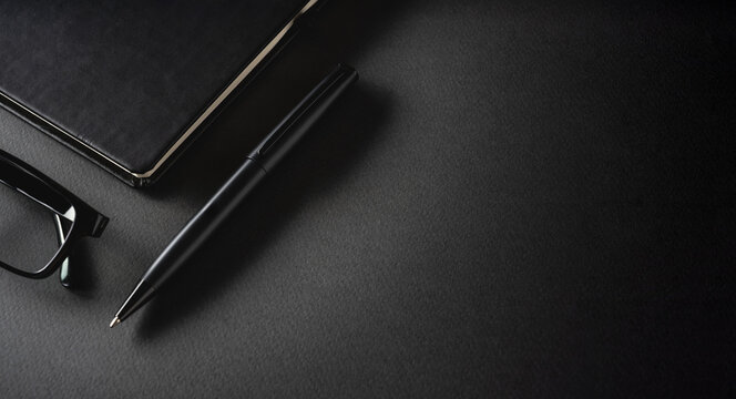Top view of ballpoint pen, glasses and notepad lying on dark gray table