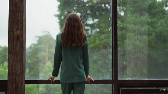 Sad corporate employee looks at rain behind window. Lady top manager thinks about lost chances for company growth in office. Woman with depression disorder