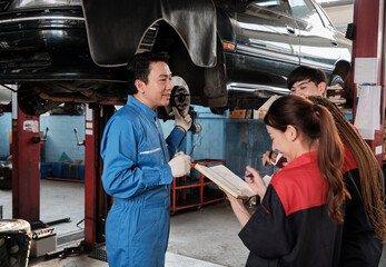 Asian male professional automotive engineer supervisor describes car wheel and suspension repair work with mechanic worker staffs team in fix service garage, specialist occupations in auto industry.