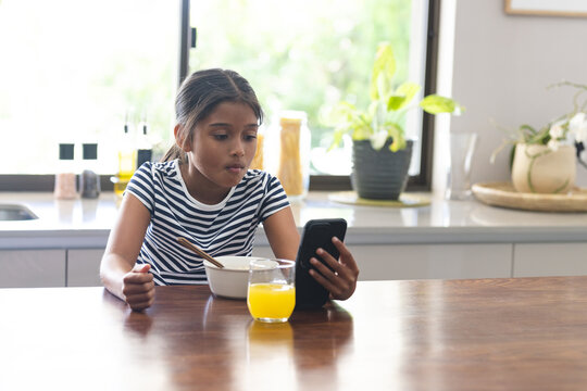 Biracial girl has breakfast at home, focused on her phone