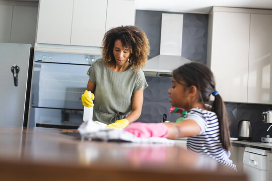 Biracial mother cleans the kitchen counter with her daughter, with copy space