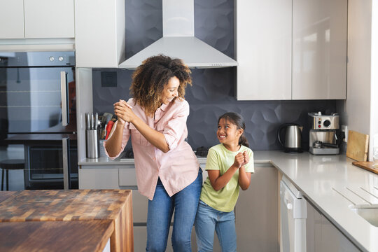 Biracial mother and daughter enjoy a dance in a modern kitchen at home