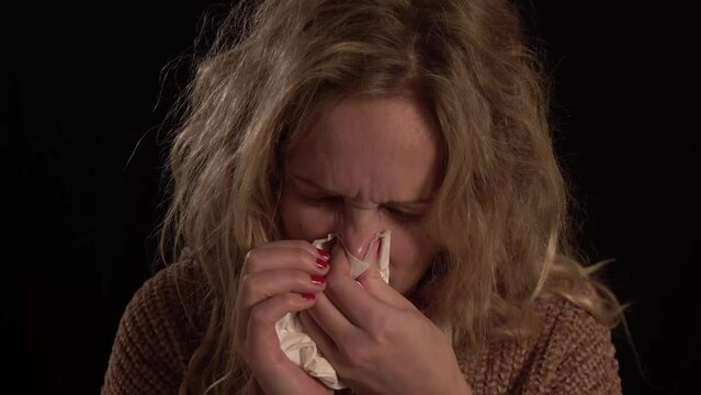 A young european blond women is blowing her nouse. She is sick. She has a runny nose and flu. She is disheveled and looking very sick.