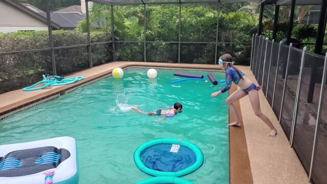 Young girl with swimming goggles jumps in the home pool in slow motion
