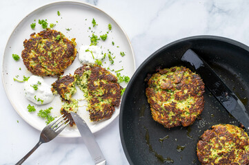 Greek zucchini fritters with herb dip on a plate and in a frying pan