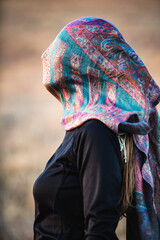Profile portrait of an adult woman with a scarf on head that covers her face in an autumn...