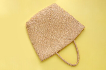 Brown wicker woven bag or straw bag on yellow background. Top view with copy space. Summer travel concept. 