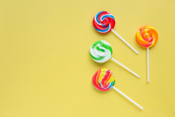 Colorful lollipops, different colored round candy on sticks on yellow background. Flat lay, top view