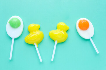 Bright yellow duck shaped candies and duck egg shaped candies on light green background. Flat lay, top view