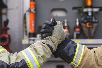 Handshake of two firefighters with a fire truck in the background