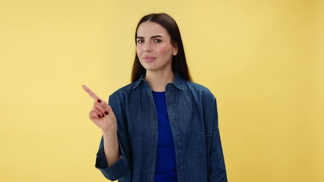 Confused female brunette pointing finger at herself and asking who me over yellow background. Caucasian woman in casual denim shirt rejecting some unfounded accusations to her side in studio.