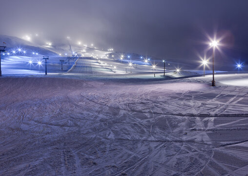 A snowy landscape with lights and ski lift tracks