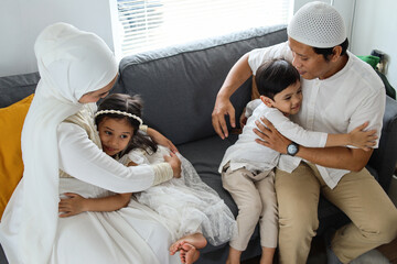 Happy Muslim children hugging their parents during Eid Mubarak while sitting together on the sofa in the living room. 