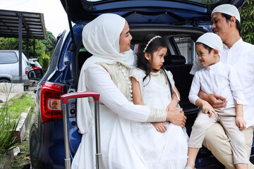 Happy Muslim family sitting in the car trunk ready to go on holiday. Mudik lebaran at Eid moment.