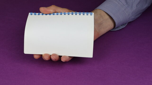 Mano che tiene piccolo quaderno ad anelli, sullo sfondo una scrivania. serie di foto.