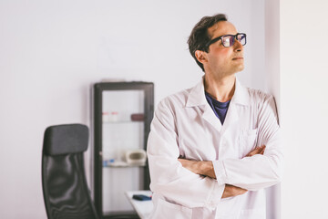 An adult male Caucasian scientist in glasses and a white coat stands and looks forward against the backdrop of a laboratory