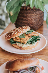 Close-up of a divided plate with bagel burger with eggs, chicken, vegan, on pink plate and on a wooden table