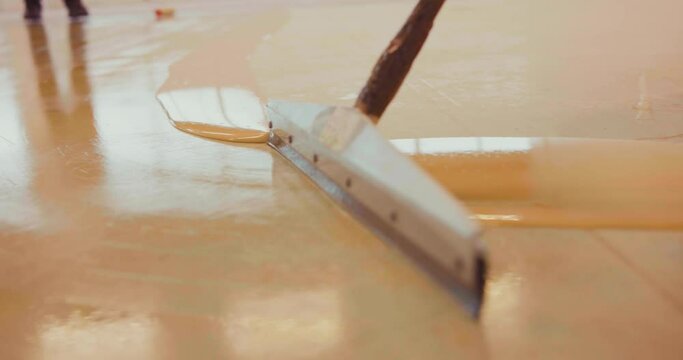 Slow-motion of a  worker applying a primer support layer for epoxy resin with a floor squeegee