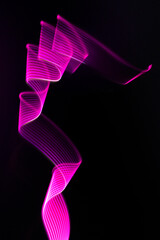 Pink, purple neon wave of light as curls or swirl with stripes on black background, vertical. Abstract background with dynamic line in motion, light painting, light effect in modern style.